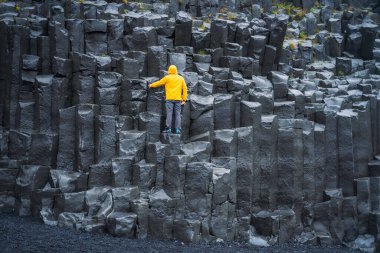 Sarı ceketli adam Reynisdrangar Bazalt sütunlarına bakıyor Reynisfjara Sahili, İzlanda.
