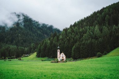 Bulutlu bir günde Ranui 'deki St. Johann Kilisesi, Dolomite Alpleri, Vilnoss Vadisi, Güney Tyrol, İtalya. Sis, çam ağacı ormanında gevşiyor..