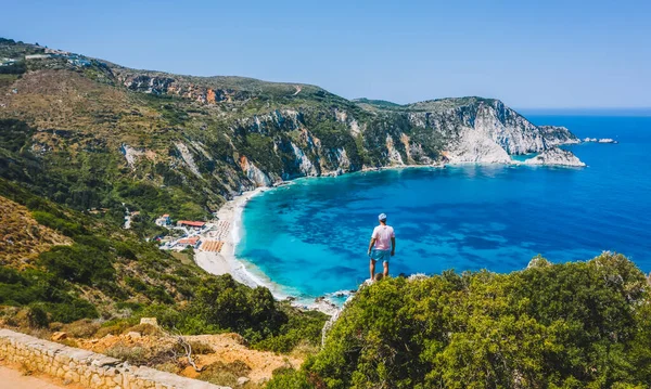Bir kayanın tepesinde duran adam heyecan verici bir özgürlük duygusuyla Petani Sahili 'ne bakıyor. Kefalonia İyonya Adası, Yunanistan.