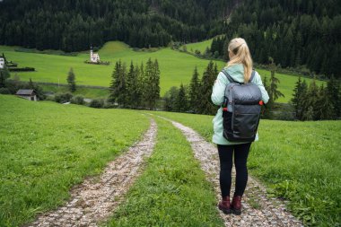 Val di Funes Vadisi, Dolomitler, İtalya, Avrupa 'daki St. Johann Kilisesi' ne yürüyüş yolunda sırt çantalı bir kadın..