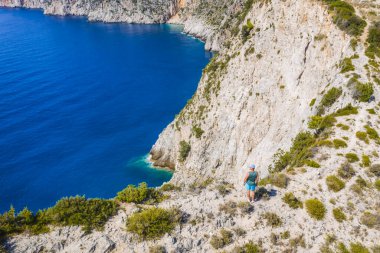 Yunanistan 'ın Cefalonia İyon adasındaki Assos köyüne yakın güzel ve pitoresk kayalık sahillerin uçurum kenarındaki insan gezginin havadan çekilmiş fotoğrafı..