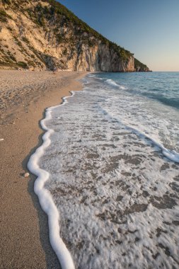 Yunanistan 'ın Lefkada İyon adasındaki Agios Nikitas köyü yakınlarında gün batımında Milos sahilinde el sallayın. İyi akşamlar altın ışık. Seyahat Konsepti.