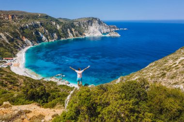 Bir kayanın üzerinde duran adam, heyecan verici bir özgürlük duygusuyla el kaldırıyor, Petani Sahili 'ne bakıyor. Sefalonya Adası, Yunanistan.