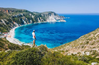 Bir kayanın tepesinde duran adam heyecan verici bir özgürlük duygusuyla Petani Sahili 'ne bakıyor. Kefalonia İyonya Adası, Yunanistan.
