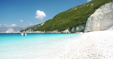 Muhteşem Fteri plajı, Kefalonia, Yunanistan. Turkuaz mavisi bir tekne ve ön planda beyaz çakıl taşı plajı..