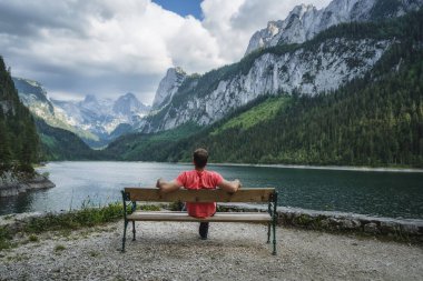 Dachstein Dağları 'nın önündeki bankta dinlenen adam Avusturya' daki Gosau Gölü 'ne yansıdı..