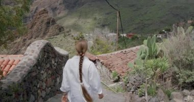 İspanyol köyü Masca Gorge, Tenerife 'yi keşfeden genç bir kadın. Sokakta yürüyen beyaz gömlekli turist kızı takip ediyor. Kanarya Adaları, İspanya. Çarpıcı bir manzara..