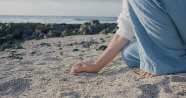 Genç bir kadın tropik sahilde beyaz kum tutuyor. Tenerife. Parmaklarınla zaman geçir. Kız sahilde oturuyor ve kumla oynuyor. Yavaş çekim.