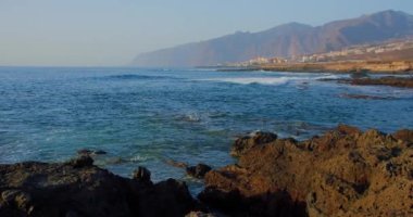 Coastline with houses, Los Gigantes cliffs in Puerto de Santiago, Santiago del Teide, Tenerife. Big waves crash on the rocky shore.