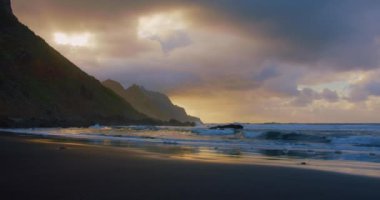 Beautiful beach with black sand and smooth waves perfect for relaxing and swimming. Reflection of sunset light on the ocean. Tenerife north. Canary Islands. Spain. Europe. Nobody.