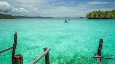Blue lagoon with pure clear water and clouds and small island in background. Small boat comming in. Pan film.