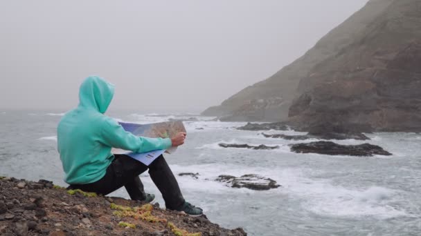 带着狗的旅行者在巨浪面前拿着地图飞溅到岩石海岸 陡峭的火山山脉耸立在远足的路上 佛得角 圣安涛岛 4K镜头 — 图库视频影像