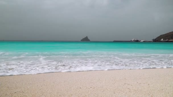 碧绿的海浪慢吞吞地滚向背景是巨大岩石的白色沙滩 — 图库视频影像