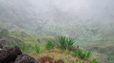 Santo Antao adasının tozlu ve yemyeşil manzarası. Dağ yamaçları agave bitkileriyle kaplıdır. Vadideki yerel bir köy. Cape Verde 'deki Santo Antao adasında muhteşem yürüyüş yolları. 4k video.
