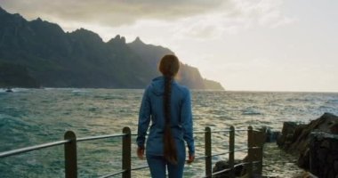 Girl enjoying the ocean view, breath deeply, early morning, new day. Young woman meditates. Concept of nature, health, solo activity.
