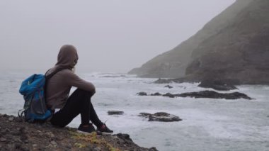 Tourist female admiring powerful waves splashing into rocky coastline. Huge volcanic mountains rugged on the trekking path. Santo Antao Island, Cape Verde. 4K footage.