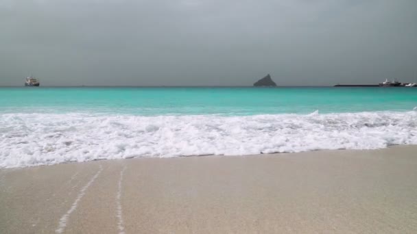 碧绿的海浪慢吞吞地滚向背景是巨大岩石的白色沙滩 — 图库视频影像