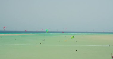 Wide shot showing group of kite surfer kiteboarding on waves of Atlantic Ocean in Playa Esmeralda, Fuerteventura, Canary Islands, Spain. Azure calm ocean waves. Picteresque spectacular cinematic 4k