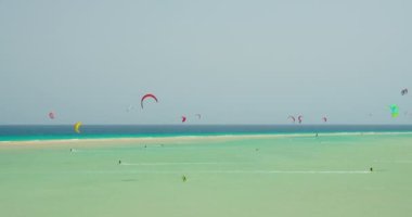 Kitesurfing on the tropical beach of Playa Del Mal Nombre, Fuerteventura, Canary Islands, Spain. Azure calm ocean waves. Picteresque spectacular cinematic. People engaged in kiteboarding turquoise sea