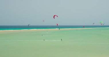 Kiters and surfers cut the waves of Atlantic ocean on the coast of Canary Islands. Extreme sports in Playa de Sotavento de Jandia, Fuerteventura, Spain. Large group of athletes.