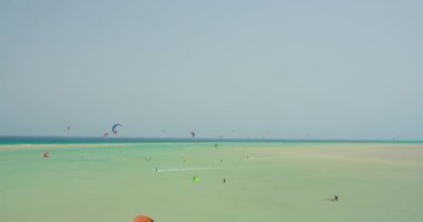 Wide shot showing group of kite surfer kiteboarding on waves of Atlantic Ocean in Playa Esmeralda, Fuerteventura, Canary Islands, Spain. Azure calm ocean waves. Picteresque spectacular cinematic 4k