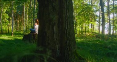 Sarışın kadın ormanda meditasyon yapıyor. Kızın dikiz aynası kütüğe oturur. Ormanda yeşil çimenler. Özfarkındalık kavramı. Ağır çekim. Sağlıklı bir yaşam tarzı. Doğayla bütünleşme. Refah.