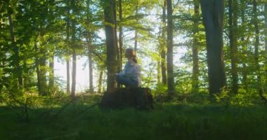 Solunum sistemini onarmak için nefes egzersizleri. Güzel bir kadın ormanın ortasında yerde oturarak meditasyon yapıyor. Genç bir kadın gözleri kapalı ormanlık alandan zevk alıyor. Yavaş çekim