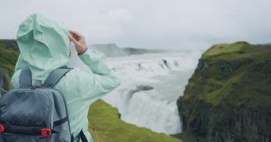 Güzel Gullfoss şelalesinin önünde sırt çantalı bir kadın gezgin. Meşhur turistik mekan ve İzlanda 'nın altın çember üzerindeki dönüm noktası..