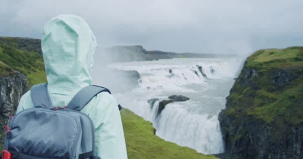 グルフォスをバックパックで見る女性旅行者ゴールデンフォールズは有名な観光名所であり ゴールデンサークルのアイスランドのランドマーク的な目的地です — ストック動画
