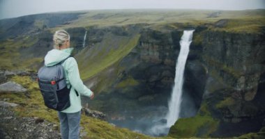 Sırt çantalı kadın İzlanda 'da Haifoss şelalesinin keyfini çıkarıyor..