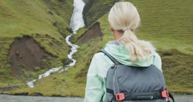 İzlanda 'nın güney kıyısındaki Fjadrargljufur yakınlarında İzlanda şelalesinin önünde sırt çantalı bir kadın turist..