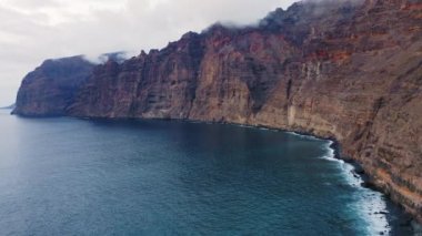 Tenerife 'deki Los Gigantes uçurumlarının havadan görünüşü. Büyük kayaların üzerinden uçmak. Sakin Atlantik Okyanusu 'nun muhteşem manzarası. Cennet muhteşem adasına bir gezi. Volkanik deniz manzarasında yolculuk. Kamera hareket ediyor