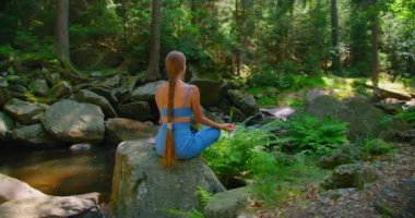 Kadın meditasyonu, zen yoga meditasyonu. Ormandaki nehir akıntısı. Nilüfer çiçekli poz veren bir kızın dikiz açısı, sağlıklı yaşam tarzı konsepti. Derin bilinçli nefes. Uzun saçlı.