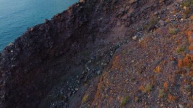 Kayalık bir sahilden derin mavi denize doğru kamera hareketi. Arka planda pelerin var. Cansız dağlar. Büyük kayaların üzerinden insansız hava aracı uçuşu. Atlantik Okyanusu 'nun sakin derin sularının muhteşem manzarası. Havadan