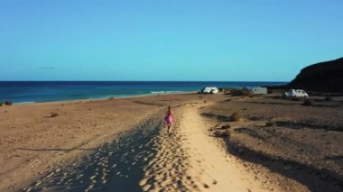 Kum tepeciğinde yürüyen bir kadın. Özgürlük için. Kumlu sahilde tatil, Costa Calma kasabası. Egzotik tropikal bölgelerde seyahat edin. Gök mavisi okyanus. Fuerteventura, Kanarya Adaları, İspanya. Temizle