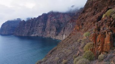 Sakin deniz manzarası, açık okyanus, büyük uçurumlar. Kasvetli bulutlu hava. Blue Sea Bay 'de gün batımı. Yaz sonrası ışıltısında koyu masmavi su. Sinematik dron görüntüleri. Tenerife adası. Kanarya Adaları