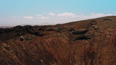 Büyük bir volkanik kraterin yamacında uçuyor. Fuerteventura Adası 'ndaki Calderon Hondo volkanı. Kızıl, kuru, cansız, kayalık toprak Mars 'ın manzaralarına benzer. Her yere gidin. Dünya gezegeni. Mavi