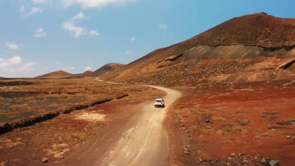山の未舗装道路上の車の後ろにドローン便 砂漠の風景の中にオフロードの空中ビュー 火山の不毛の悪い土地 目的地へ どこへでも行け 旅行の時間です フェルテベントゥラ カナリア — ストック動画