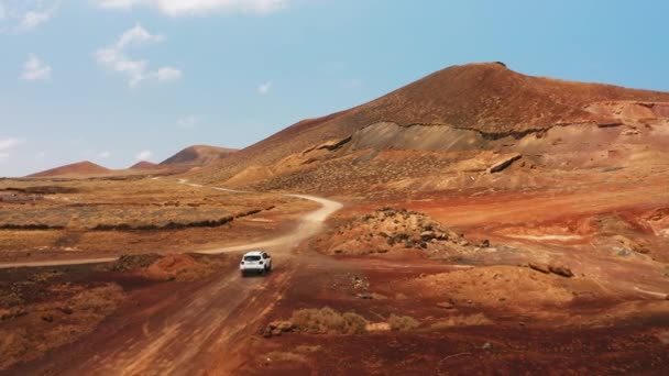 山の未舗装道路上の車の後ろにドローン便 砂漠の風景の中にオフロードの空中ビュー 火山の不毛の悪い土地 目的地へ どこへでも行け 旅行の時間です フェルテベントゥラ カナリア — ストック動画