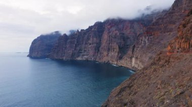 Sakin deniz manzarası, açık okyanus, büyük uçurumlar. Kasvetli bulutlu hava. Blue Sea Bay 'de gün batımı. Yaz sonrası ışıltısında koyu masmavi su. Sinematik dron görüntüleri. Tenerife adası. Kanarya Adaları