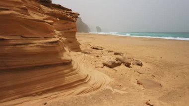 Sonsuz kum plajı üstünde insansız hava aracı uçuşu. Volkanik dağ manzarası. Gün batımında altın kum taşları. Sıcak ışık. Okyanus suyu buharlaşır. Toz, sis, sis dalgaların üzerinde yükseliyor. Fuerteventura, Kanarya