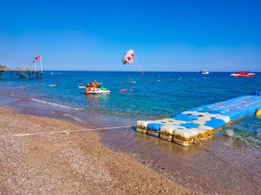 Tekirova, Antalya, Türkiye - 11 Mayıs 2021: Deniz kıyısı yakınlarındaki mavi gökyüzünde paraşütle atlama. Parasailing, Türkiye 'de turistler arasında popüler bir eğlence etkinliğidir. Sadece yazı işleri için..