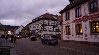 Eguisheim, Alsace, Fransa - 30 Aralık 2021: Turistler renkli yarı ağaçlı evler arasında Grand Rue caddesi boyunca yürüyorlar