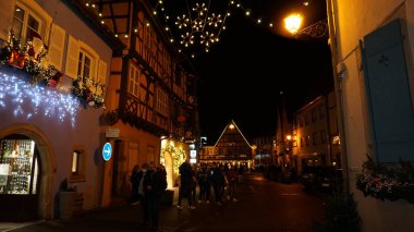 Eguisheim, Alsace, Fransa - 30 Aralık 2021: Turistler renkli yarı ağaçlı evler arasında Grand Rue caddesi boyunca yürüyorlar