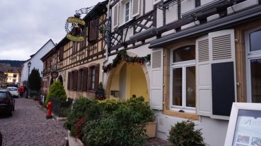 Eguisheim, Alsace, Fransa - 30 Aralık 2021: Turistler renkli yarı ağaçlı evler arasında Grand Rue caddesi boyunca yürüyorlar