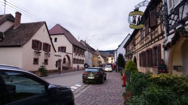 Eguisheim, Alsace, Fransa - 30 Aralık 2021: Turistler renkli yarı ağaçlı evler arasında Grand Rue caddesi boyunca yürüyorlar