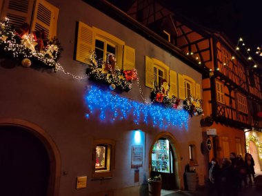 Eguisheim, Alsace, Fransa - 30 Aralık 2021: Turistler renkli yarı ağaçlı evler arasında Grand Rue caddesi boyunca yürüyorlar