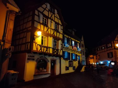 Eguisheim, Alsace, Fransa - 30 Aralık 2021: Turistler renkli yarı ağaçlı evler arasında Grand Rue caddesi boyunca yürüyorlar