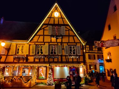 Eguisheim, Alsace, Fransa - 30 Aralık 2021: Turistler renkli yarı ağaçlı evler arasında Grand Rue caddesi boyunca yürüyorlar