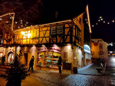 Eguisheim, Alsace, Fransa - 30 Aralık 2021: Turistler renkli yarı ağaçlı evler arasında Grand Rue caddesi boyunca yürüyorlar